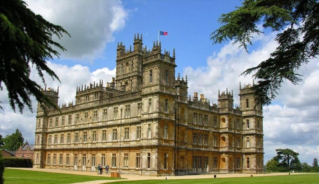 Highclere Castle, a grand stone mansion with multiple towers and spires, flies a flag.