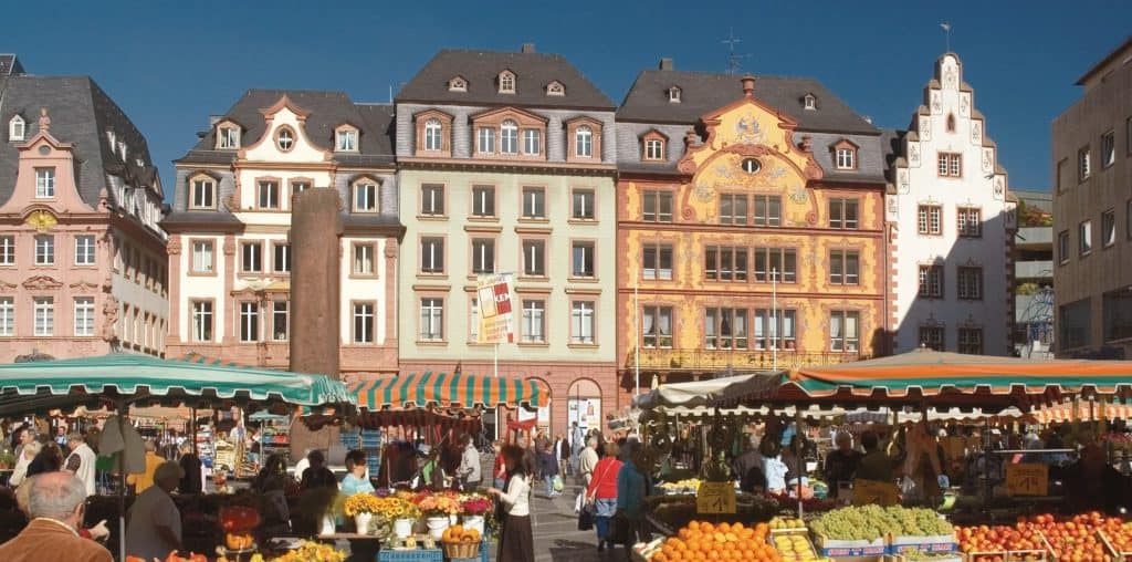 Outdoor market with colorful produce stalls in front of historic European buildings under clear.