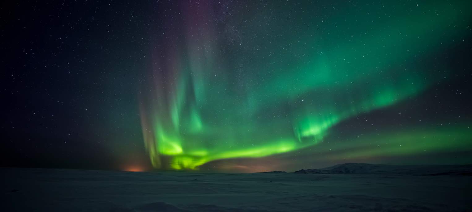 Bright green aurora borealis dancing across a dark night sky above a frozen landscape.