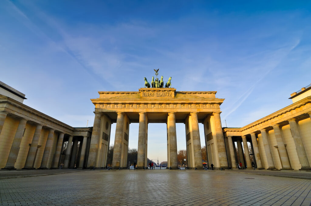 The Brandenburg Gate in Berlin stands illuminated against a blue sky, with classical columns.