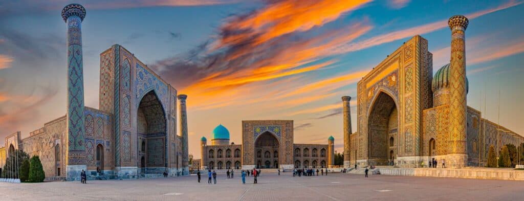 Registan square in Samarkand featuring three ornate madrasahs with blue tilework at sunset.