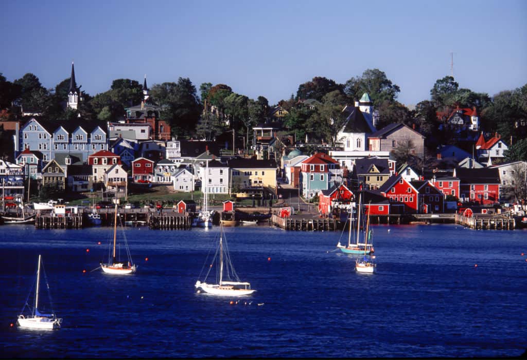 Sailboats anchored in a blue harbor with colorful waterfront buildings and church steeples.