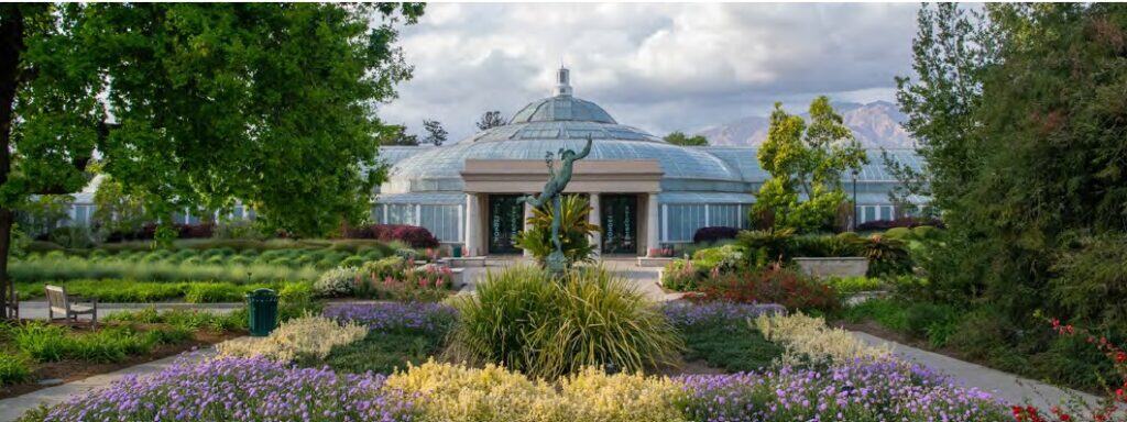 A domed conservatory building surrounded by manicured gardens with purple flowers and ornamental.