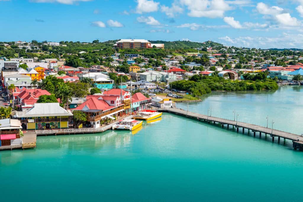 Colorful waterfront town with turquoise water, red-roofed buildings, and a wooden pier extending.