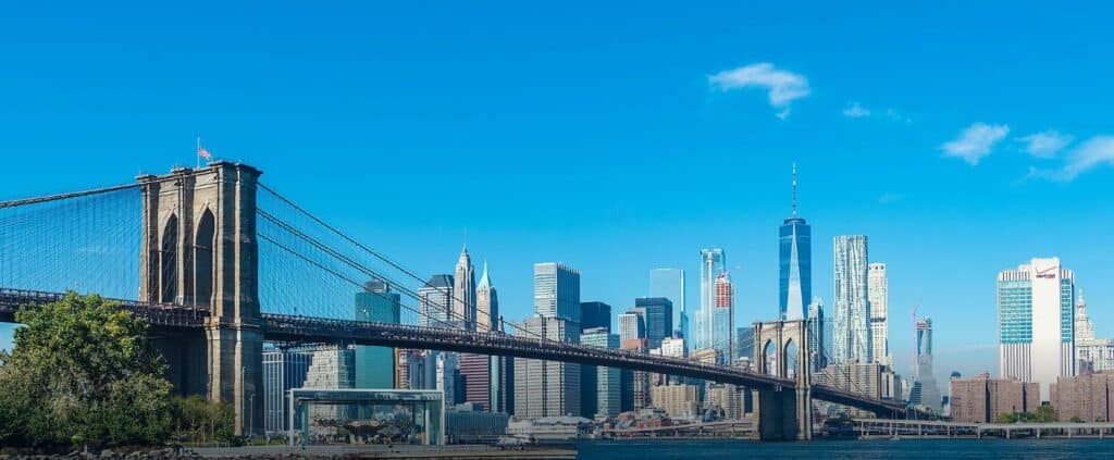 Brooklyn Bridge spans the East River with Manhattan's skyline in the background under clear blue.