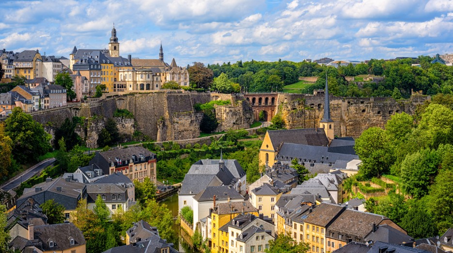 Aerial view of Luxembourg City with historic fortifications, colorful buildings, and green valleys.